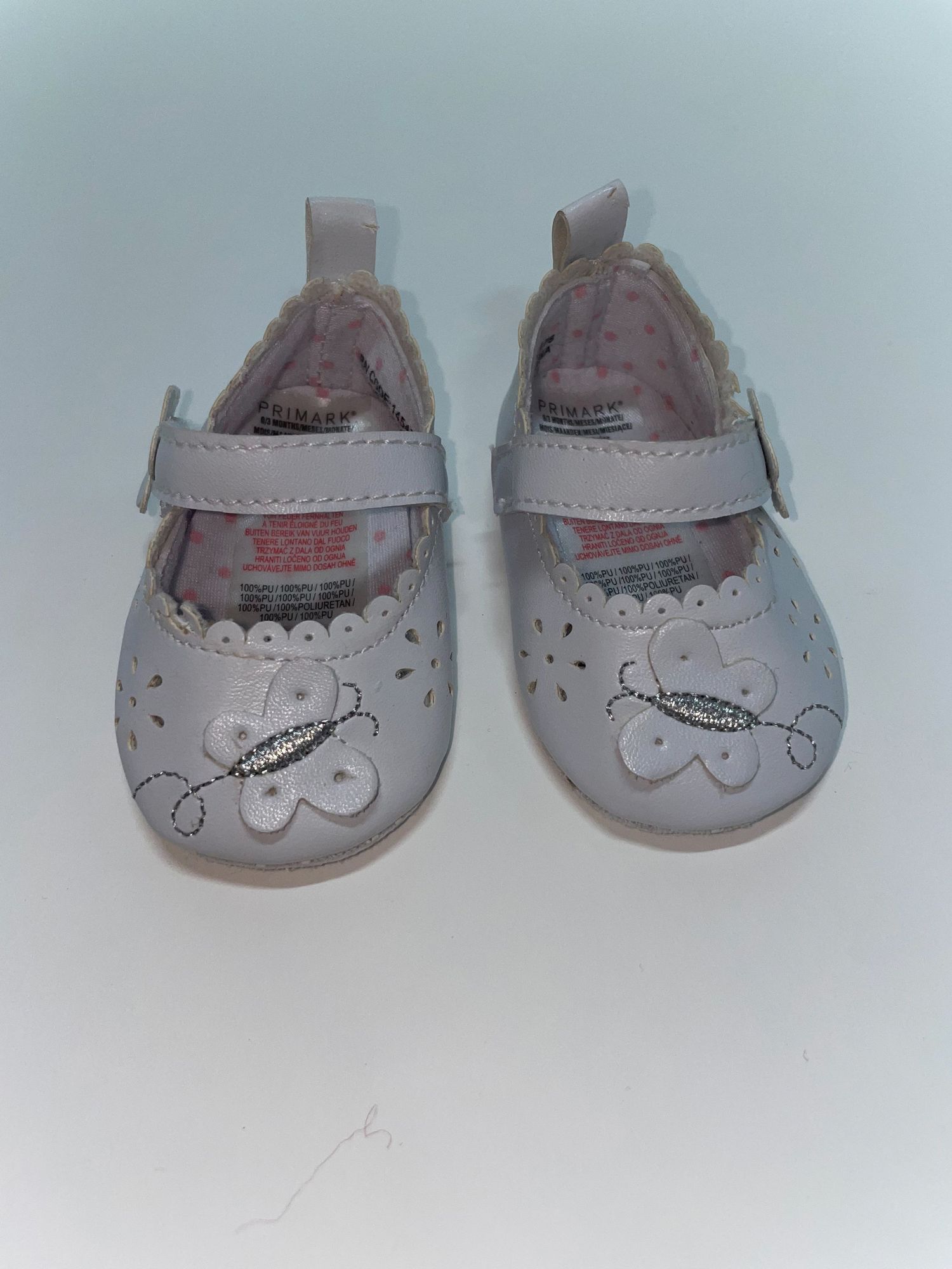 Baby shoes in light gray leather with floral cutout details and strap closure.