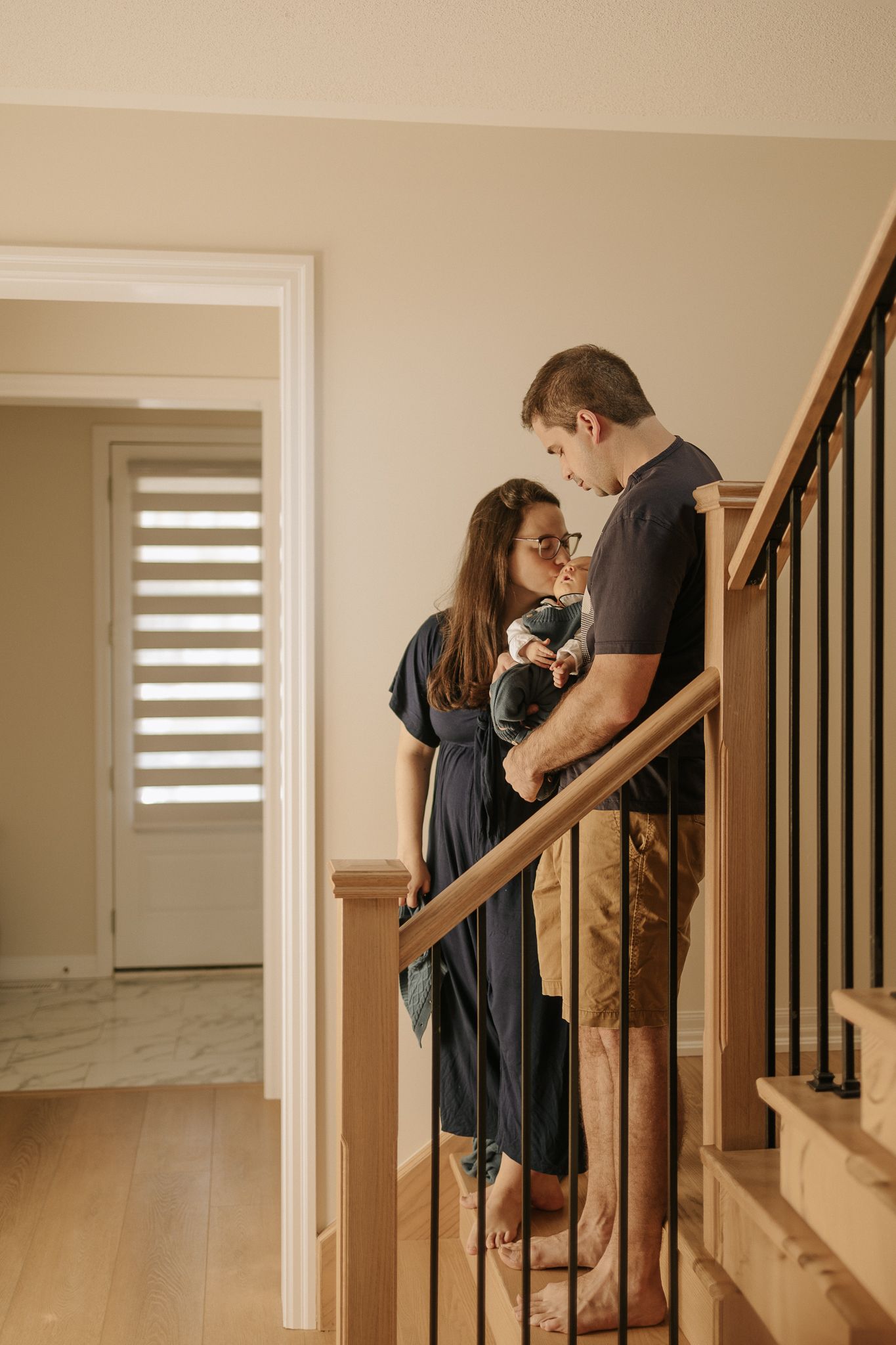 family standing in their hall, on the stairs, looking at their new born