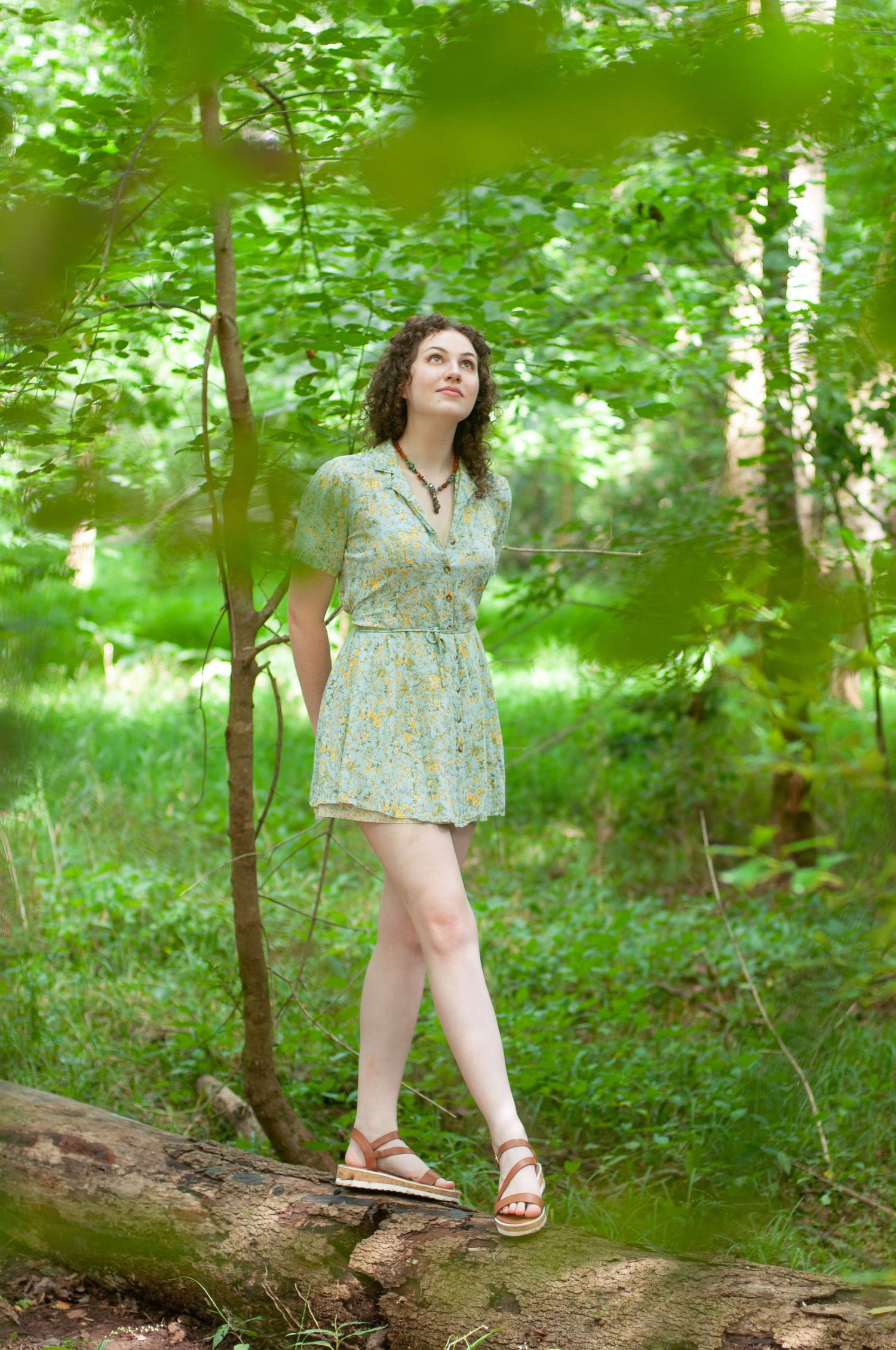 Portrait of a woman in a dress in the woods. She looks into the sun and is framed by leaves