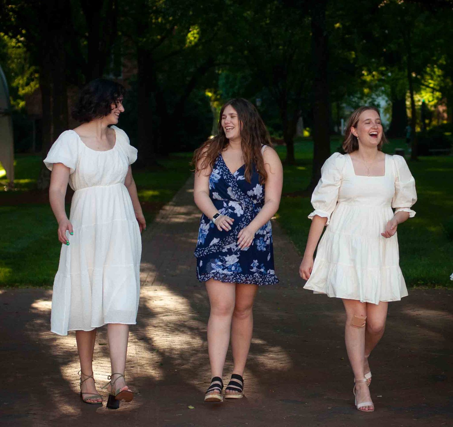 Three women in a candid and authentic photo walk down a path in dresses before college graduation