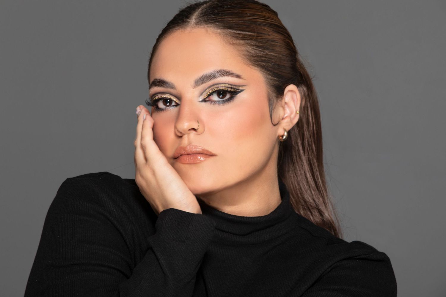 Professional beauty portrait of someone wearing a black turtleneck against gray background with dramatic makeup.