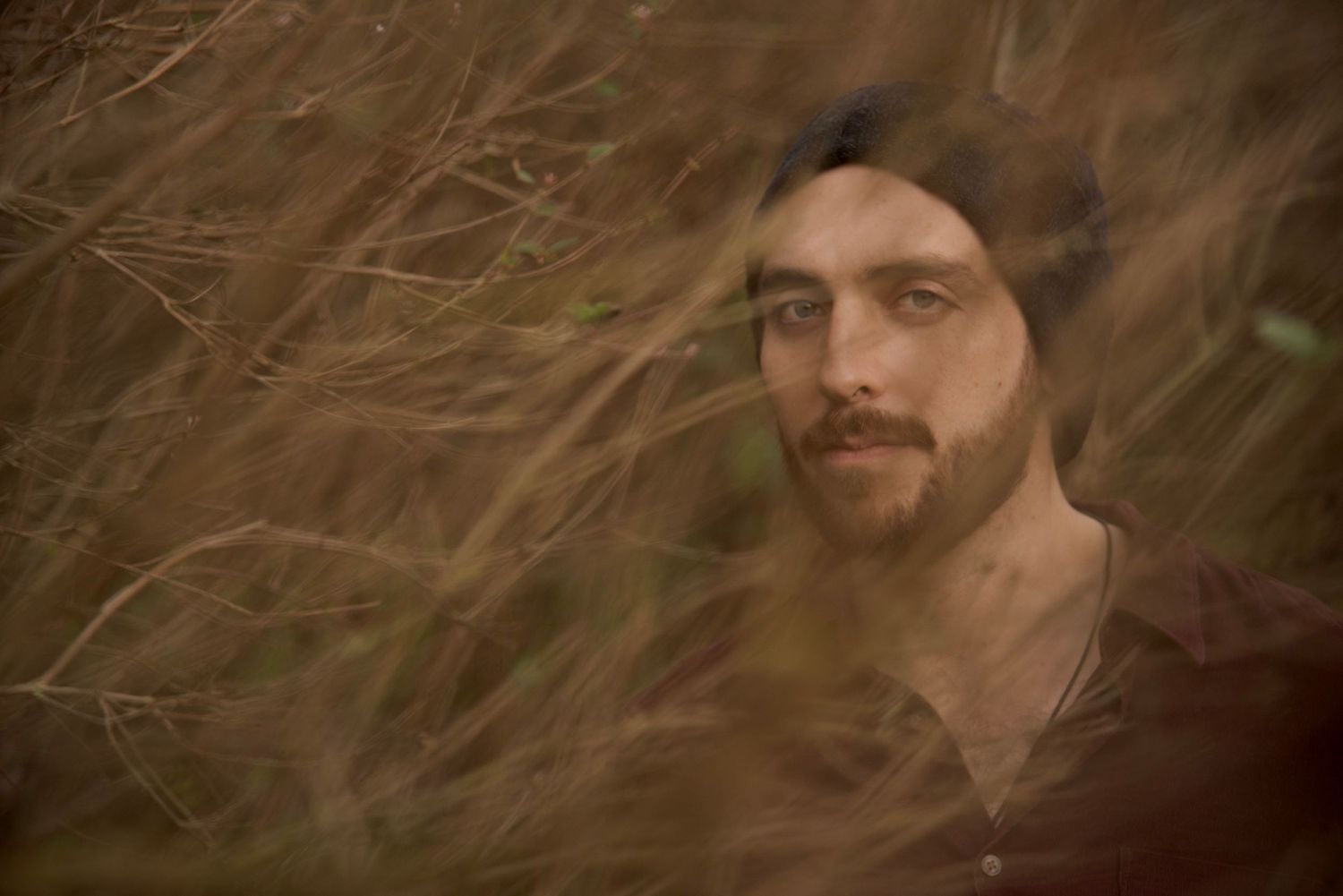 Artistic portrait photograph through autumn branches with warm moody lighting and shallow depth of field.