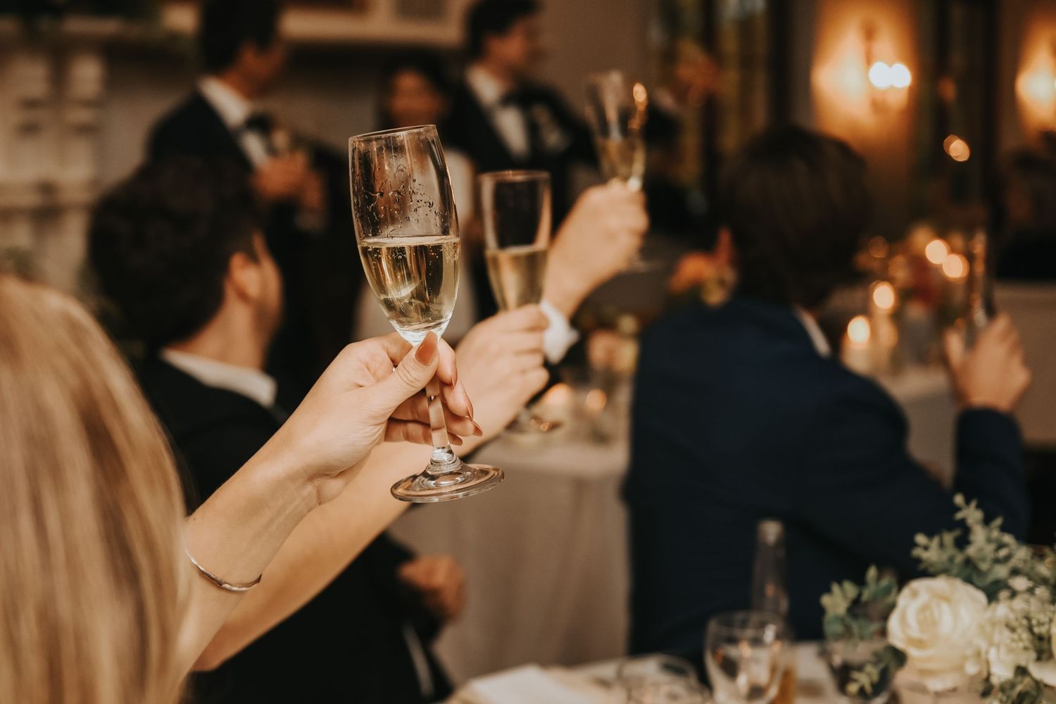 Wedding guests raise champagne glasses for a toast at an elegant evening reception celebration.