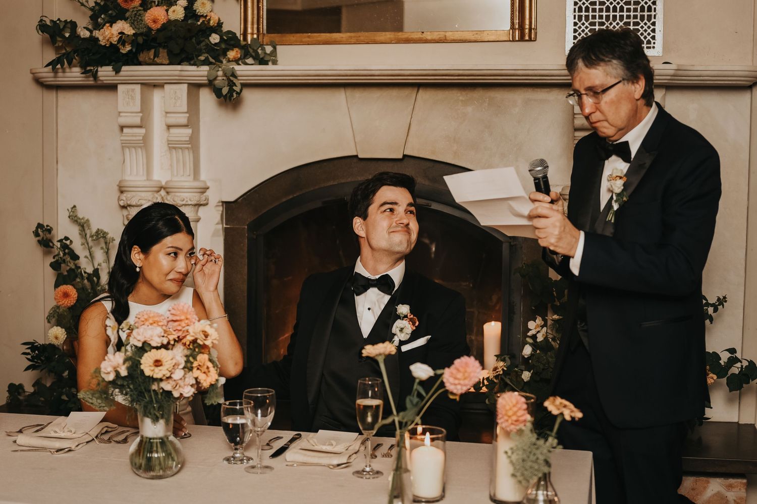 Wedding reception guests listen to a Best Man's speech during dinner at a formal event with elegant decor.