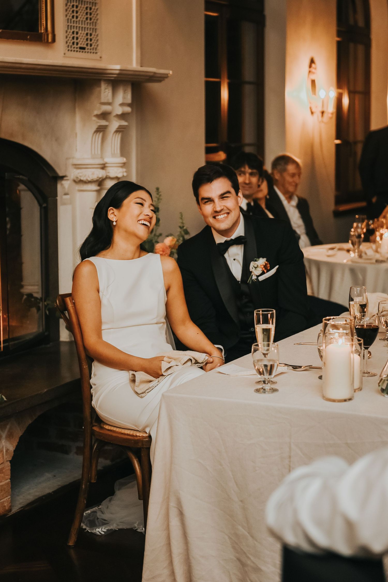 A wedding reception at an elegant venue with guests seated at candlelit tables enjoying conversation and drinks.