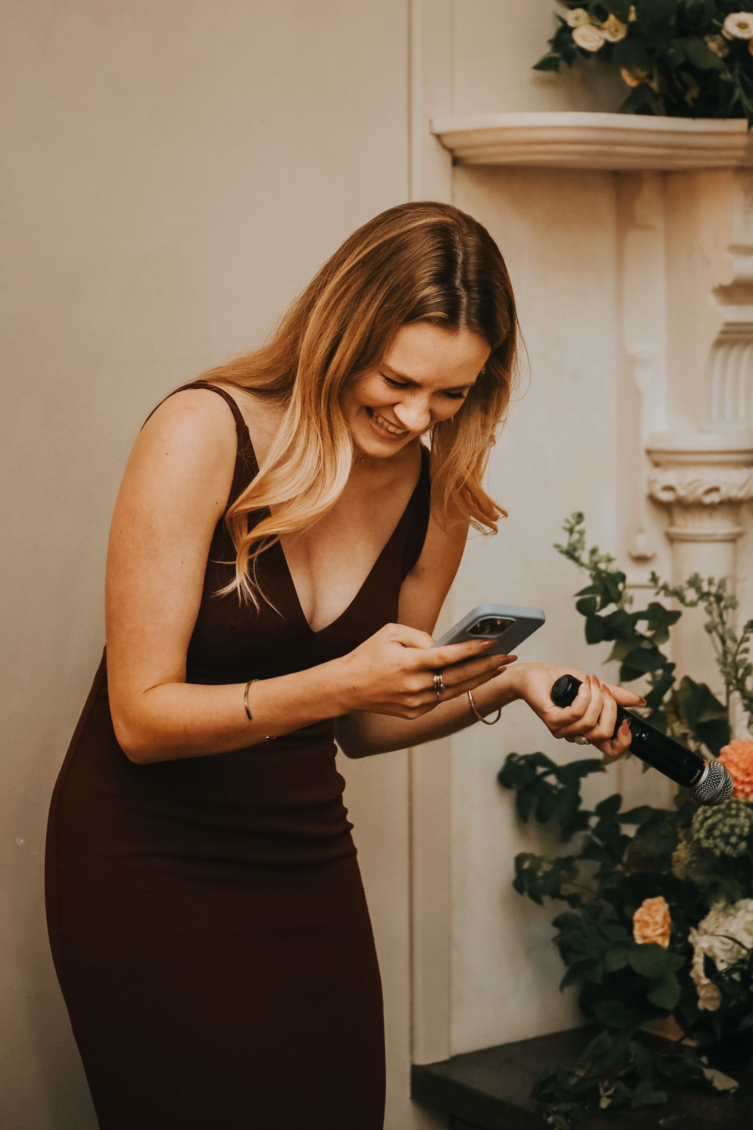 Woman in black tank top laughs while decorating Christmas tree in warm indoor setting.