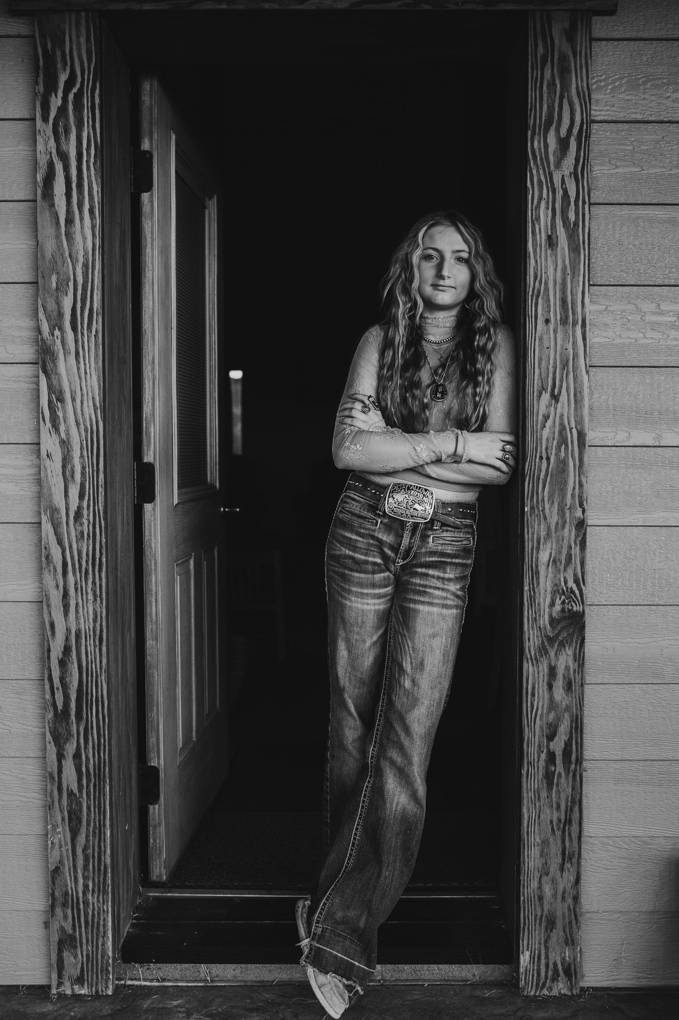 A moody black and white portrait against wooden pillars on a porch.
