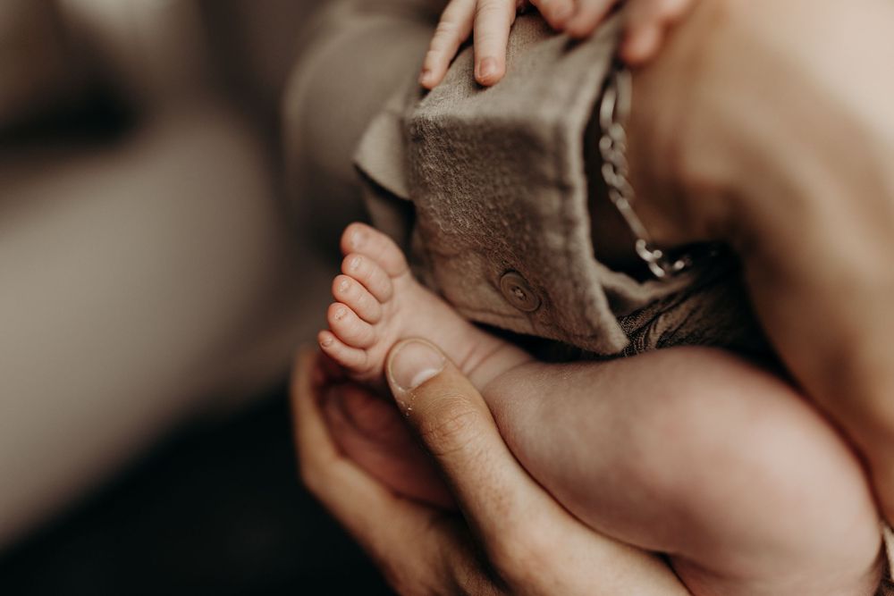 Close-up of a newborn baby's tiny feet held gently by adult hands next to soft brown booties.
