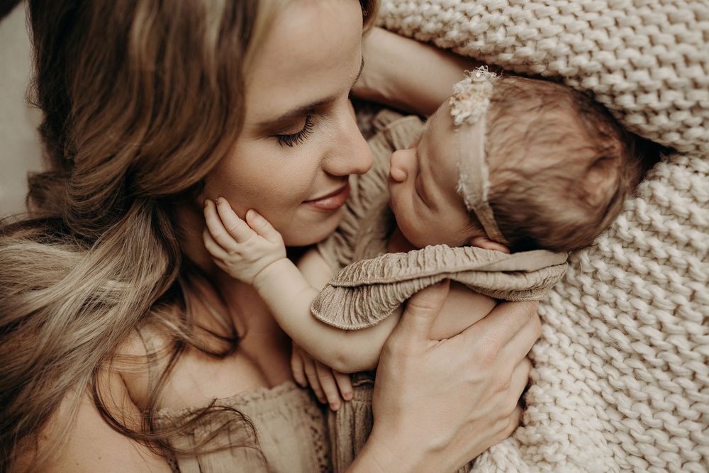 A tender moment of a mother cradling her newborn baby wrapped in a soft beige knit blanket.