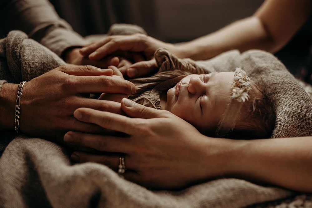 Parents tenderly cradling a sleeping newborn baby girl wearing a floral headband, wrapped in a soft blanket.