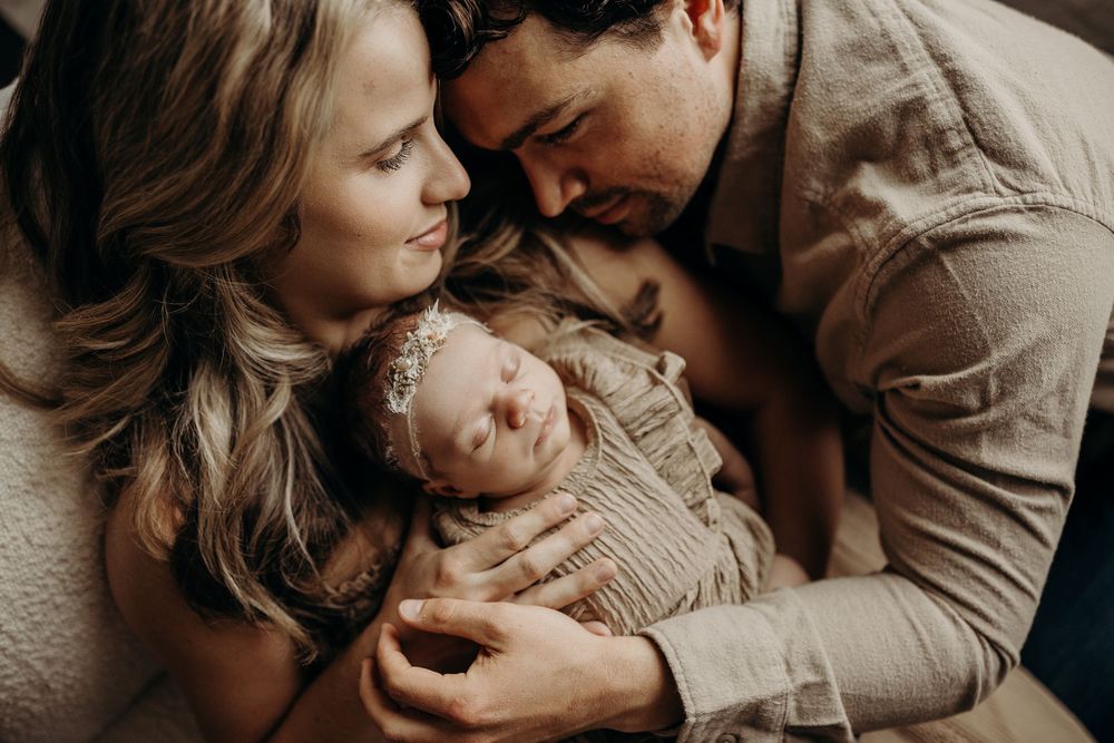 New parents tenderly cradle their sleeping newborn baby together in a warm, intimate family portrait.