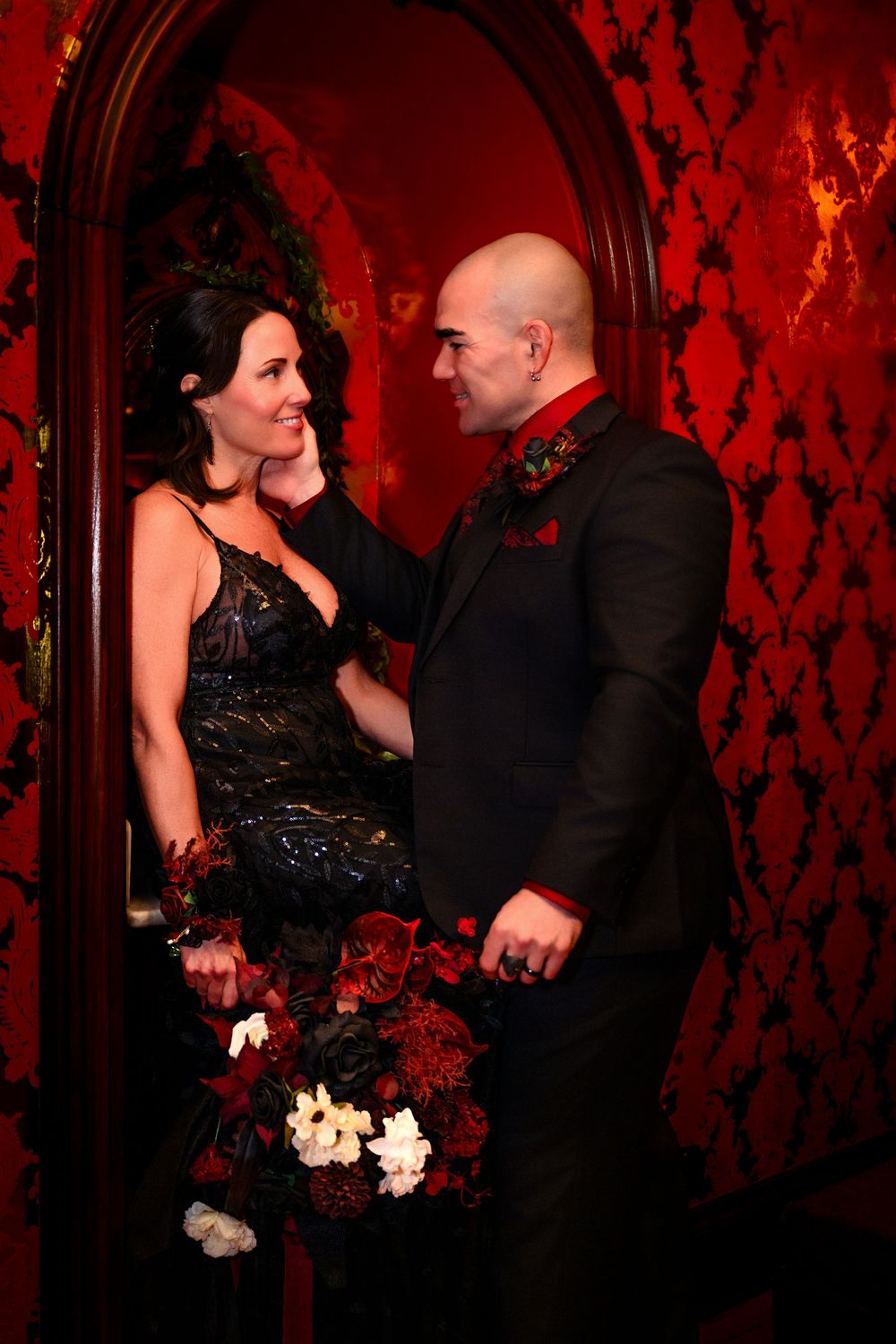 A couple in formal attire shares an intimate dance moment against a red-lit wall with dramatic lighting and shadows.