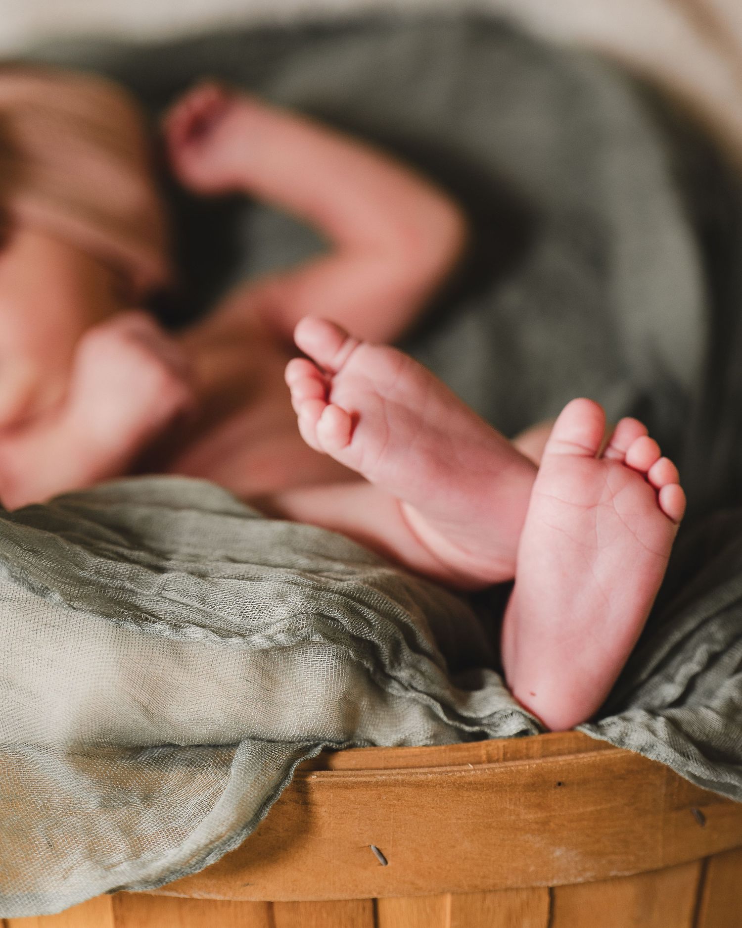 Small baby feet resting on gray bedding atop wooden surface in soft natural lighting.