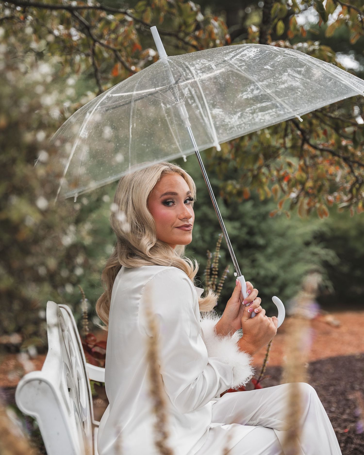 Elegant scene with clear umbrella and white clothing against autumn foliage.