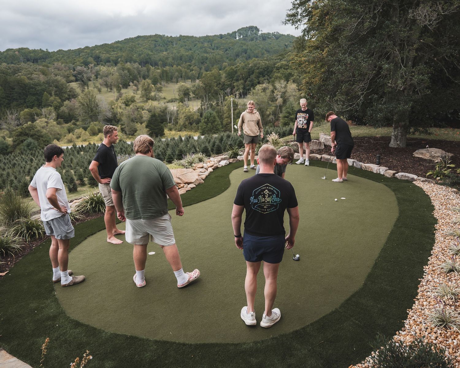 Group of people gathered on an outdoor putting green surrounded by mountain scenery.