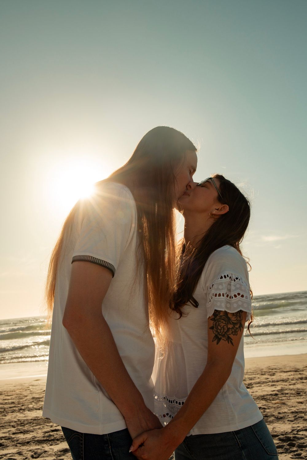 A romantic couple sharing a kiss on the beach at sunset.