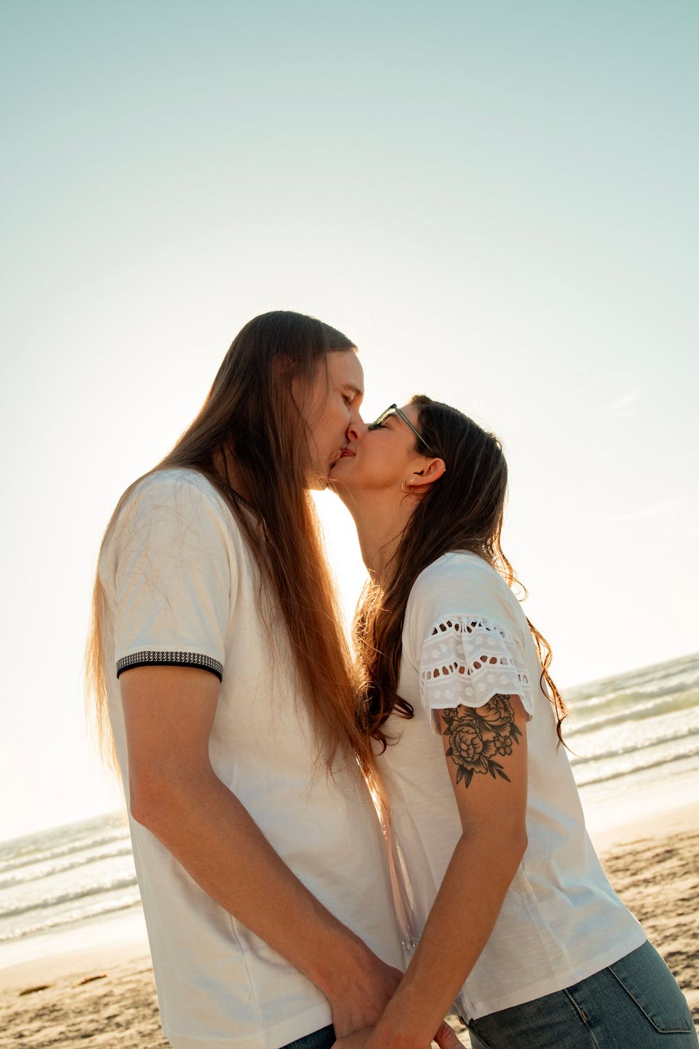 A tender moment between a couple kissing on a sunlit beach.