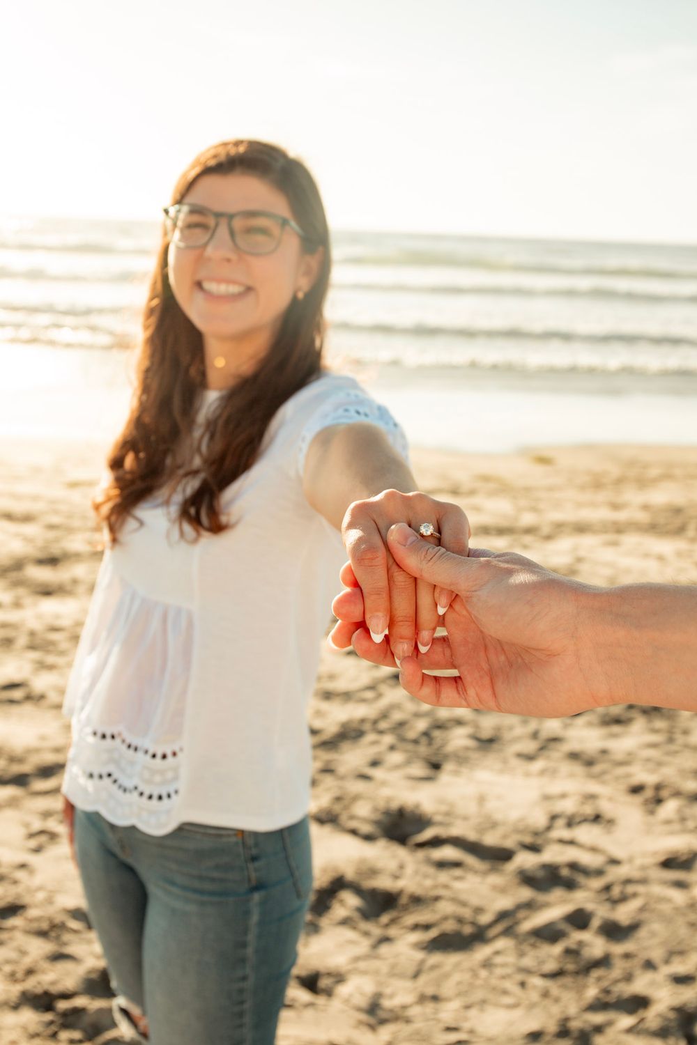A couple holds hands on a sunny beach during a romantic moment with waves in the background.