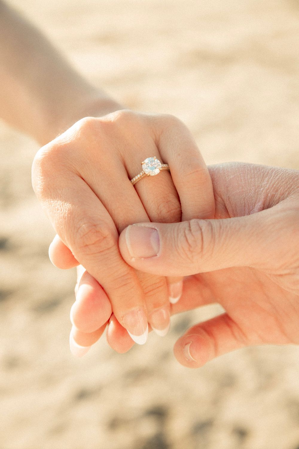 Close-up of hands holding with engagement ring sparkling in the sunlight on beach.