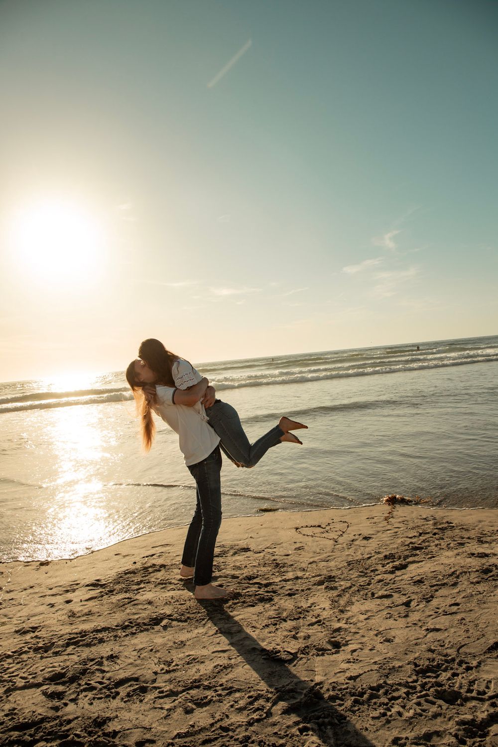 Silhouetted couple embracing and lifting on beach at sunset with ocean waves in background.