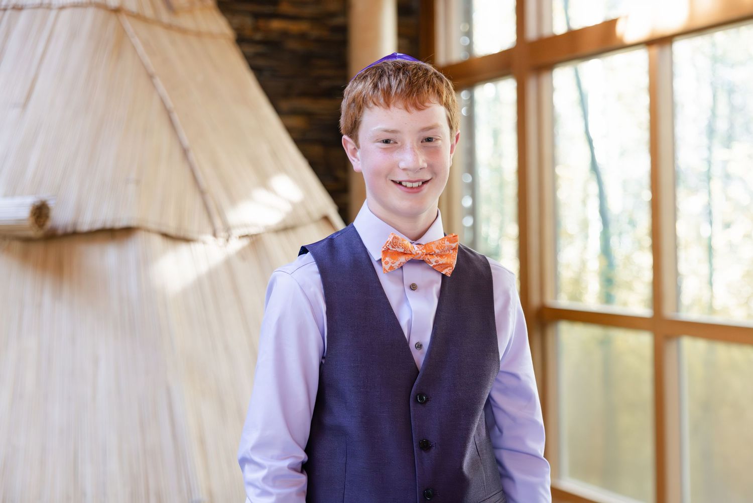 A young person wears a navy vest with an orange bow tie and white shirt at a formal event.