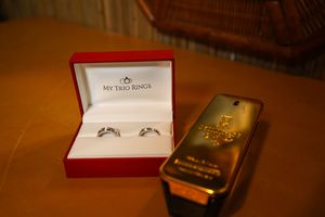 Two gold engagement rings sit alongside a white ring box and other wedding accessories on a wooden surface.
