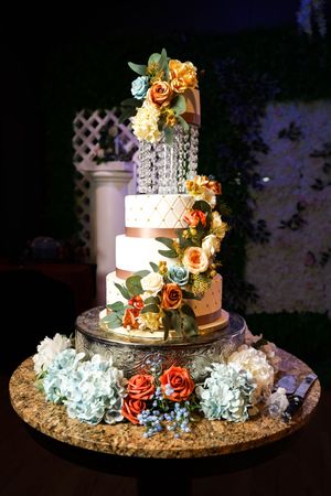 Elegant three-tier wedding cake decorated with peach roses and white hydrangeas displayed on an ornate silver stand.
