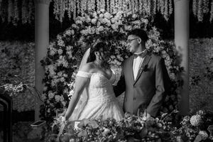 Romantic black and white wedding photography shows newlyweds under floral archways at an elegant garden ceremony.