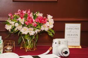 Pink and white alstroemeria flowers arranged in geometric gold vases on a dark wooden surface.