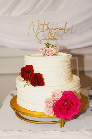 White wedding cakes decorated with pink and red roses displayed on gold cake stands.