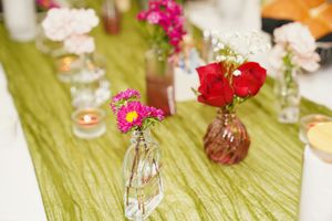 Colorful carnations in small glass vases line a green table runner at an elegant party setting.