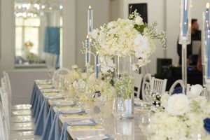 A long banquet table decorated with elegant white floral centerpieces and blue napkins for a formal wedding reception.