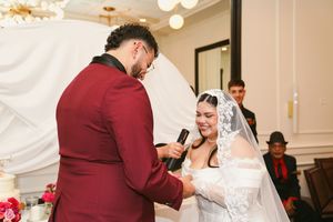 A couple in burgundy and white wedding attire share an emotional moment during their wedding ceremony.