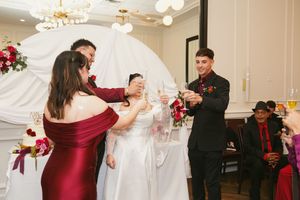 Wedding party in burgundy and black attire performing a synchronized dance move at the reception.