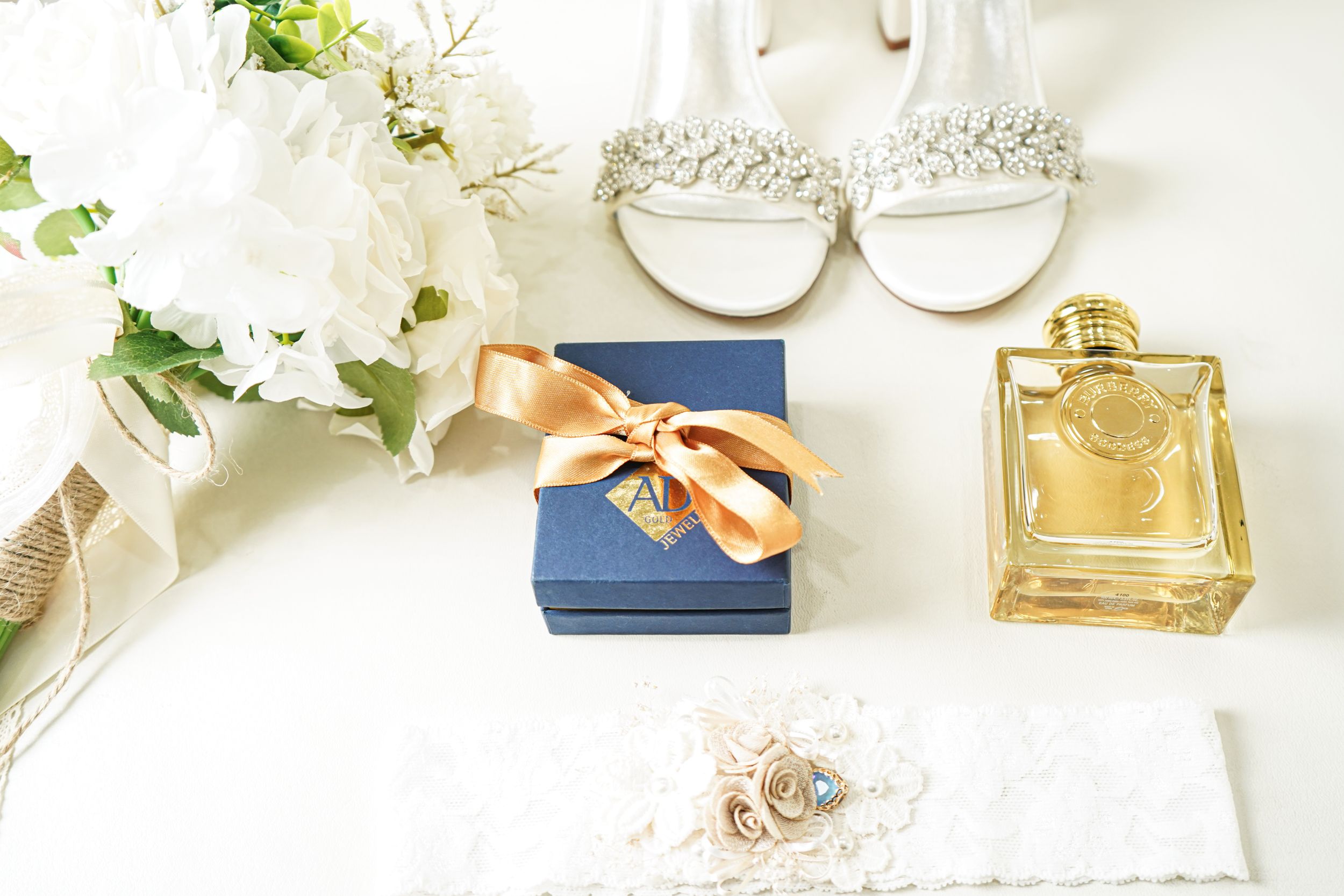 Elegant flatlay with perfume bottles, jewelry and white flowers on light surface.
