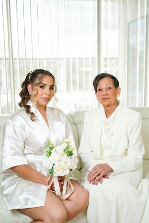 Wedding preparation scene with bridesmaids in white robes holding bouquets near window.
