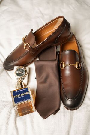 Brown leather loafers and cologne bottle displayed elegantly on white fabric.