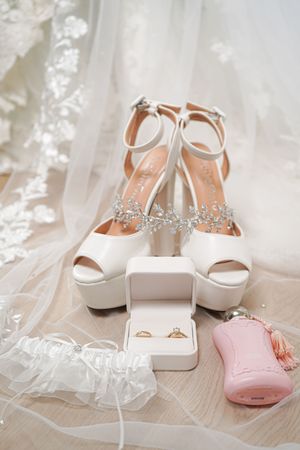 White bridal shoes with crystal embellishments and delicate lace veil arranged on a light surface.