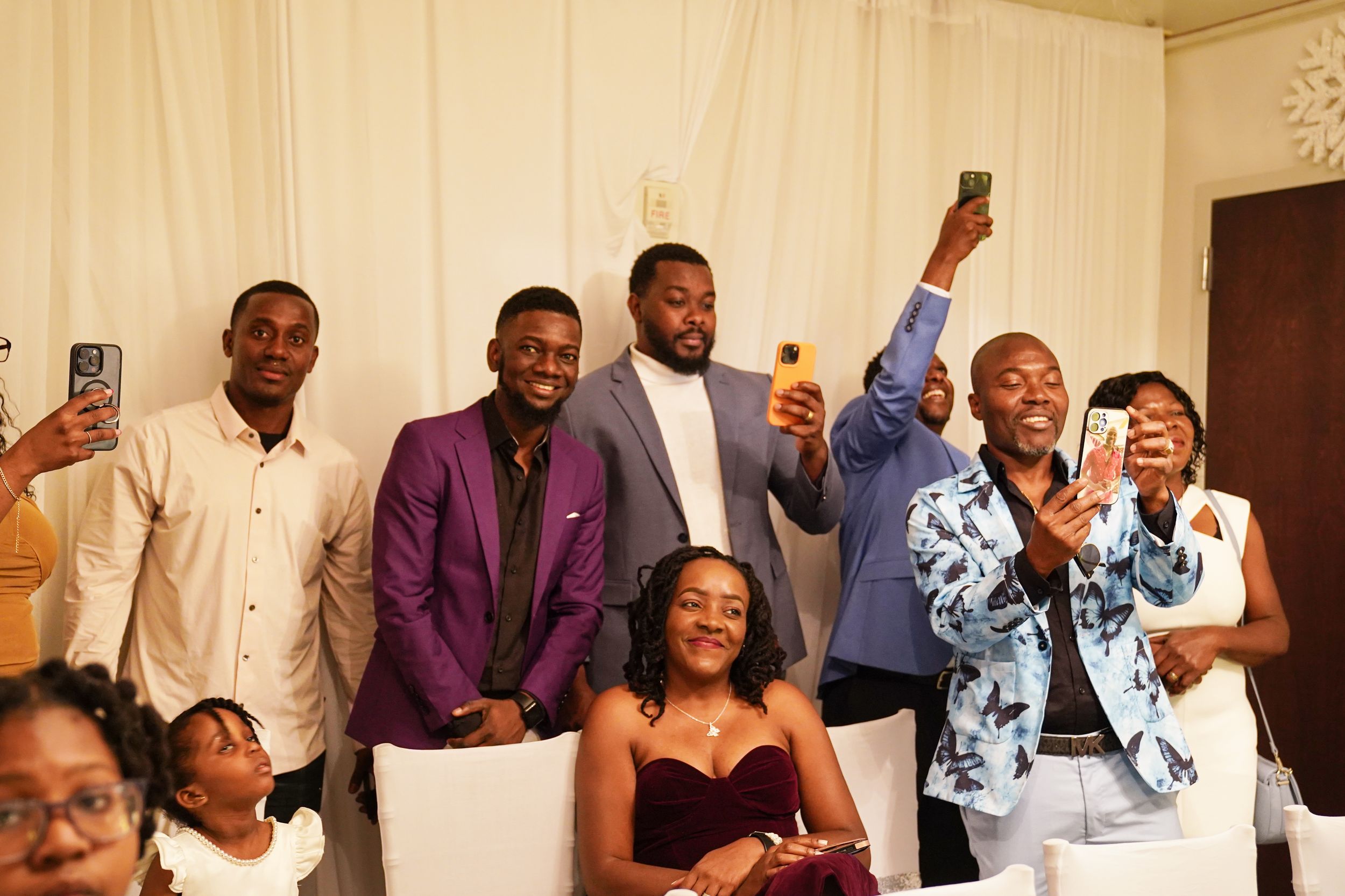 A group of wedding guests joyfully taking selfies and photos during a celebration at an indoor venue.