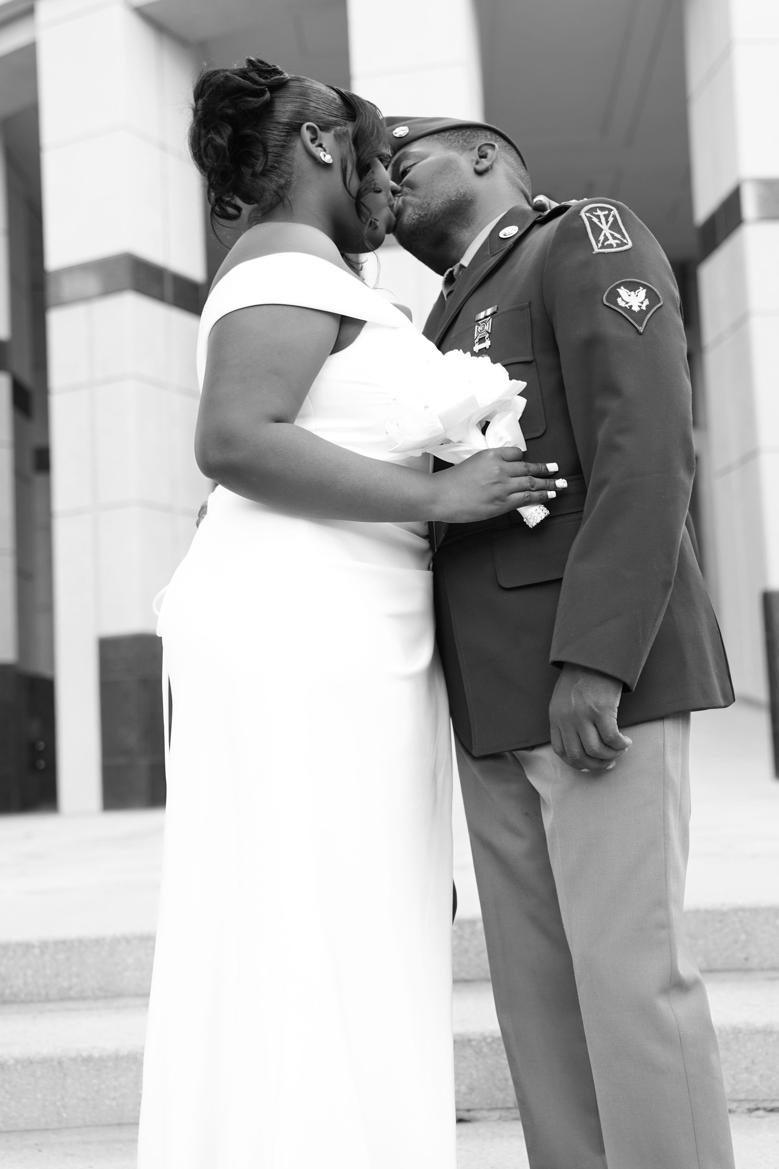 Black and white photo of a military wedding couple sharing a romantic kiss on outdoor steps.