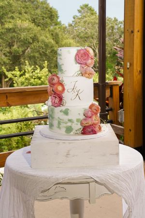 Elegant white tiered wedding cake adorned with blush pink roses displayed on white tablecloth outdoors.