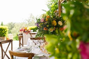 Elegant outdoor table setting with hanging greenery, floral centerpieces, and wooden chairs for garden dining event.