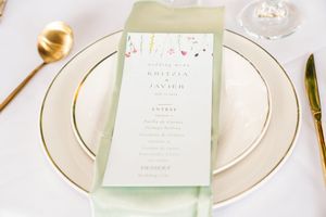 Elegant white and mint green wedding invitation suite with gold details and floral design laid out on white surface.