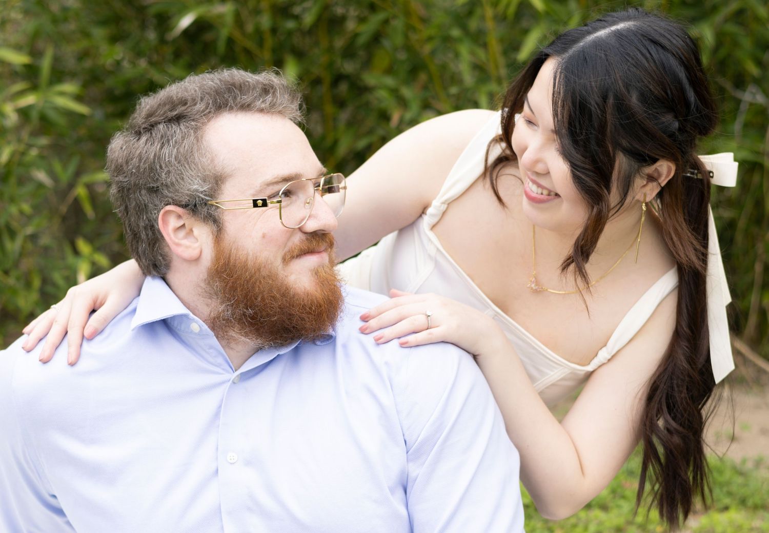 A couple shares a joyful moment together outdoors with greenery in the background.