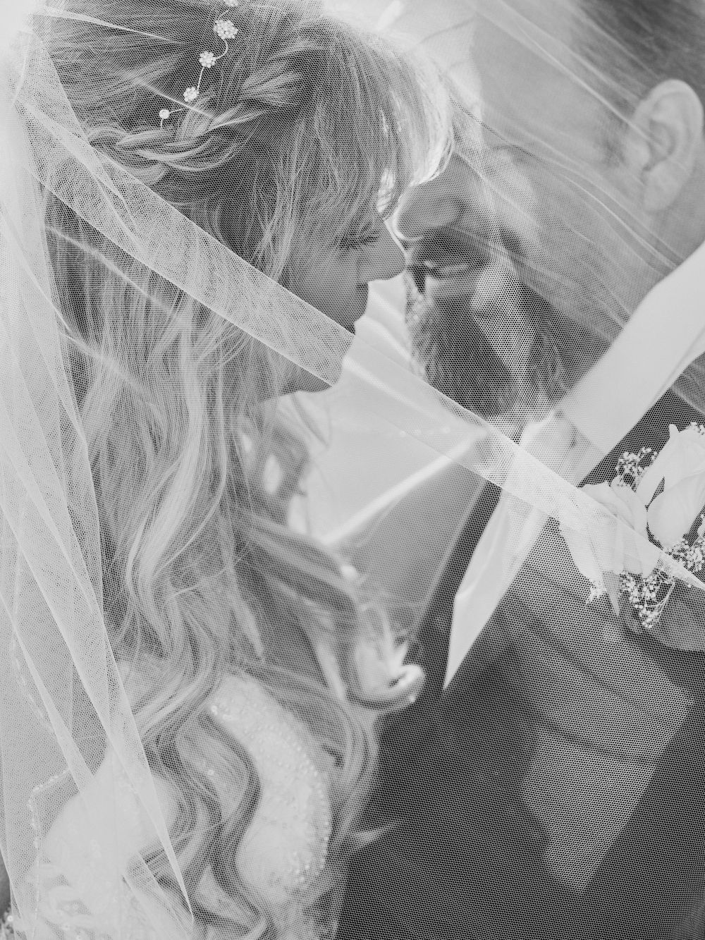 Close-up black and white wedding portrait of a bride in a delicate veil with elegant curled hairstyle.