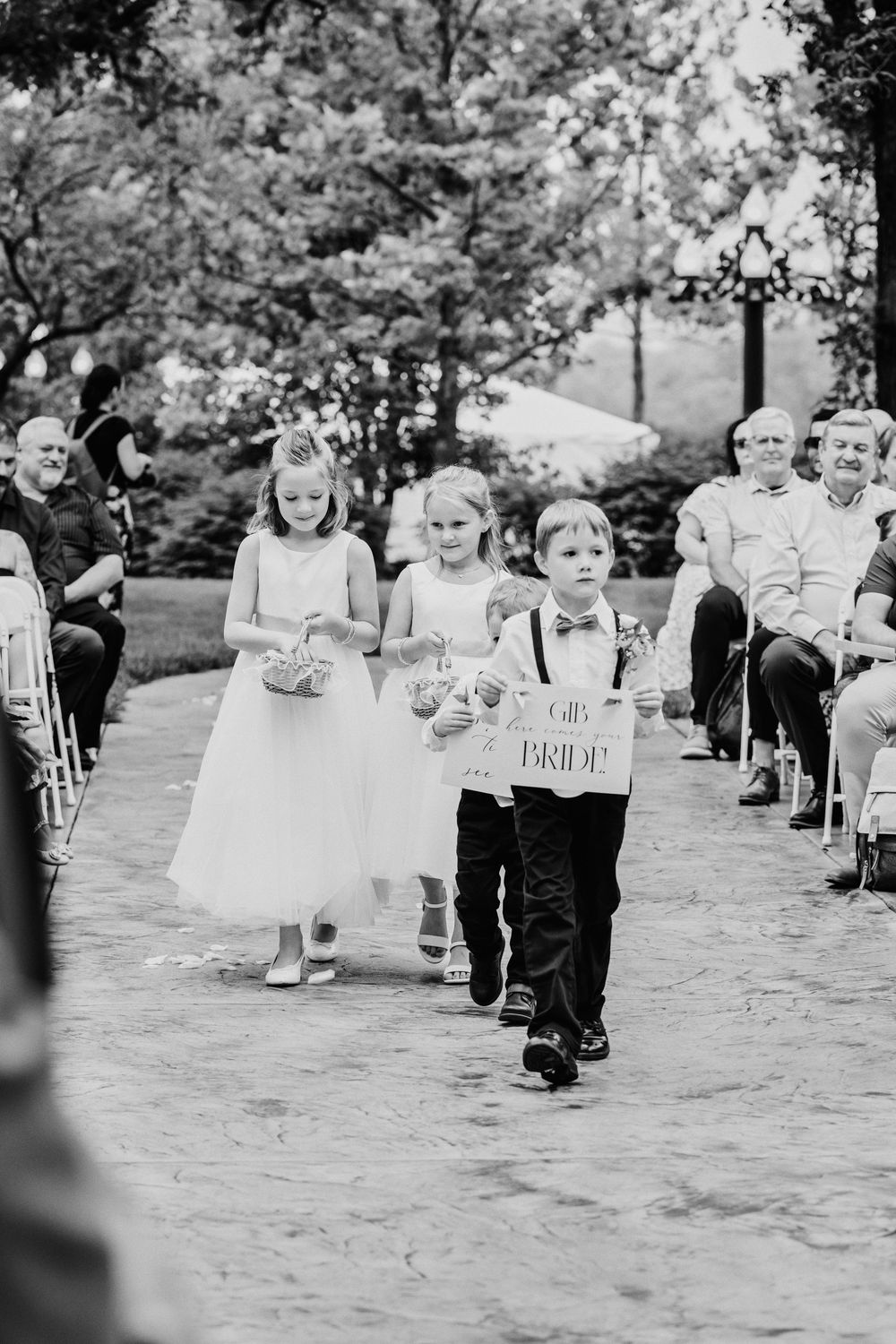 Young children walking down a pathway at a wedding ceremony holding custom signs.