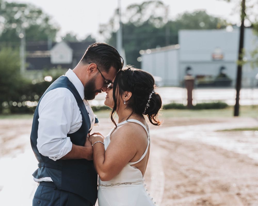 A couple shares an intimate moment together at their outdoor wedding reception while wearing white and navy blue attire.