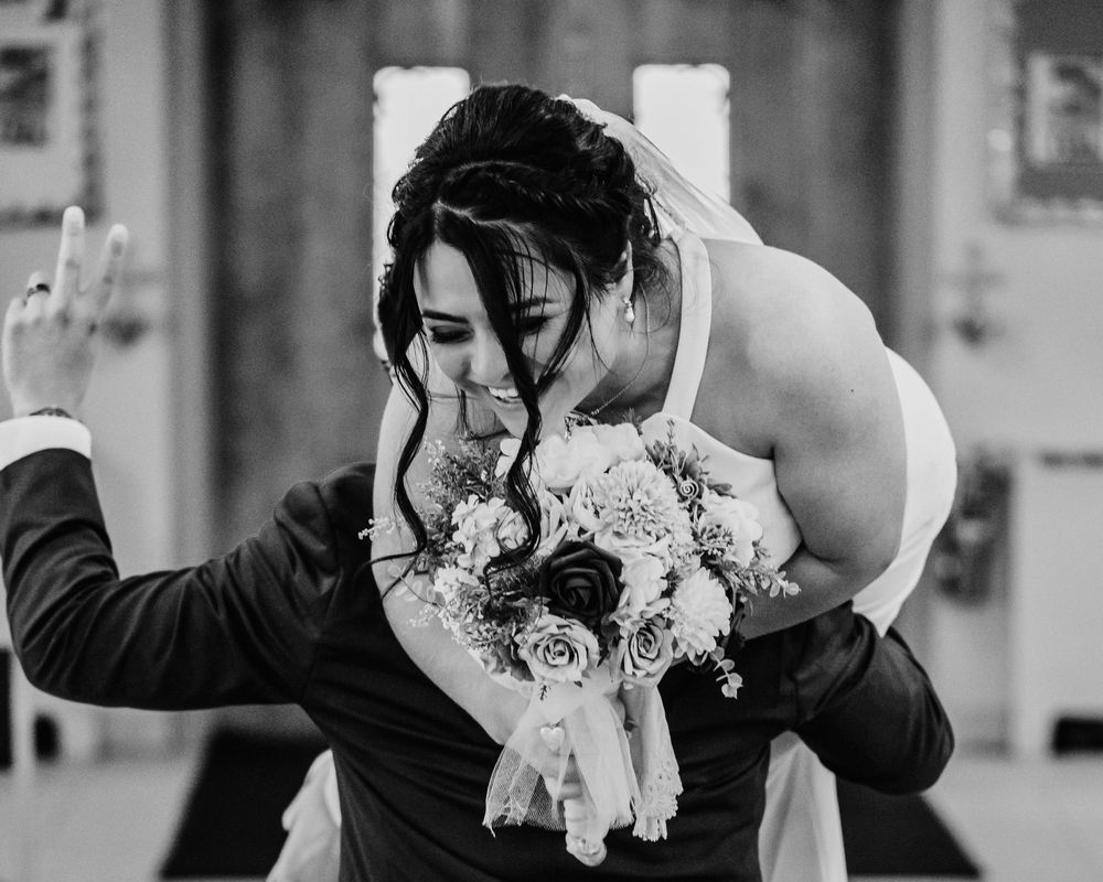 A couple shares a romantic dip kiss while holding a bridal bouquet of white and pink flowers during their wedding day.