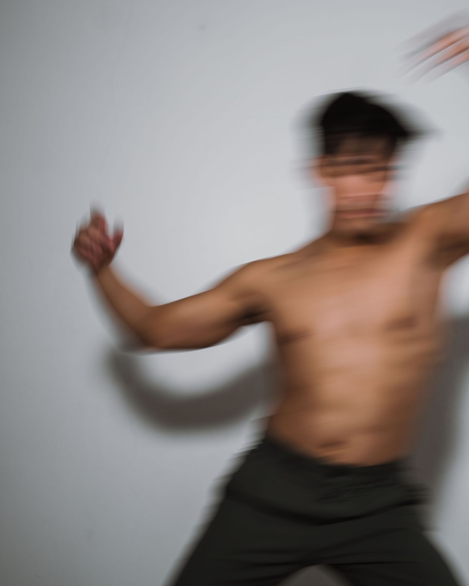 Motion blur photo of a shirtless dancer moving expressively against a white backdrop.