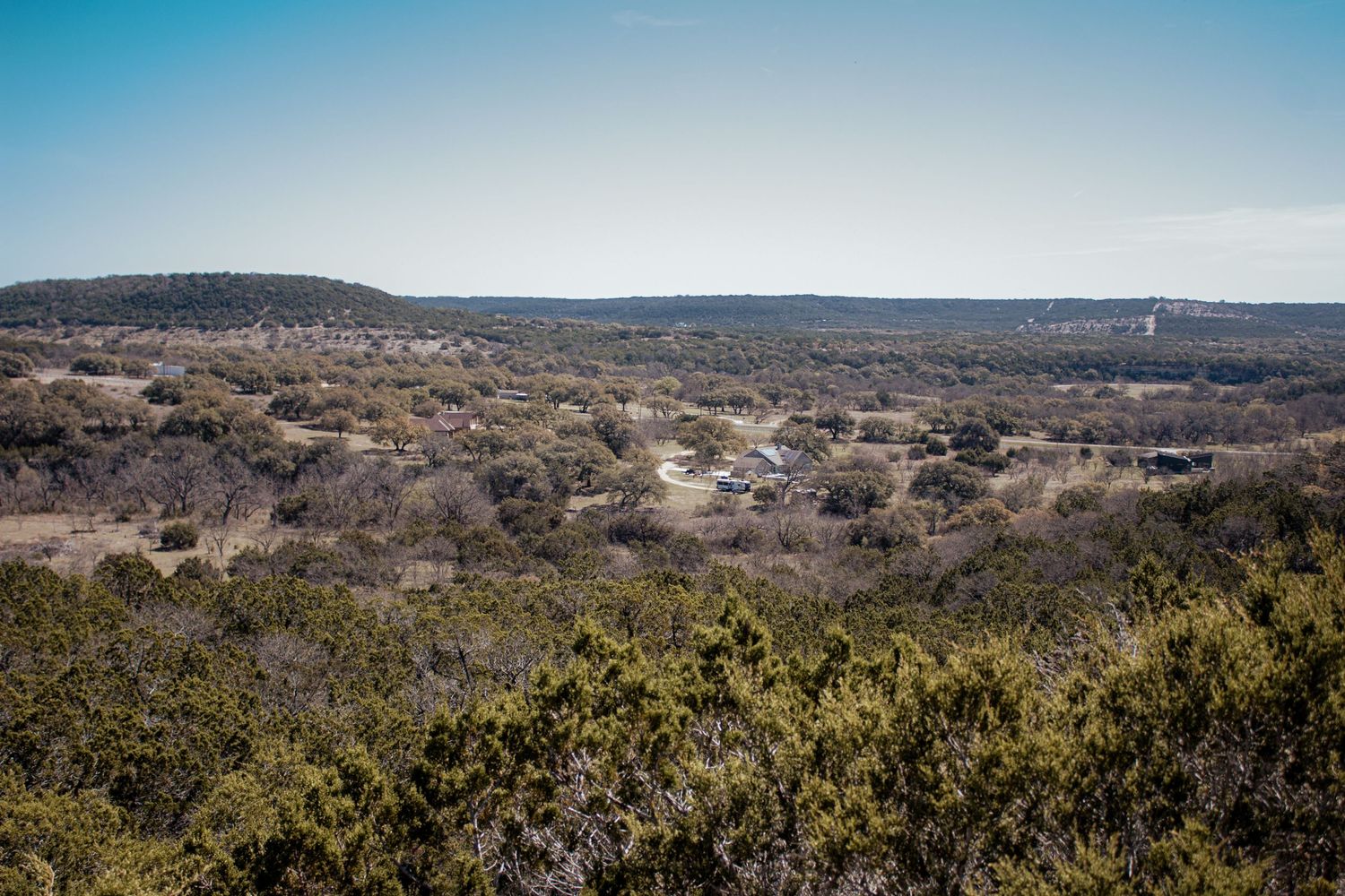 A panoramic view of rugged Texas Hill Country terrain with rolling hills and scattered vegetation stretching to the horizon.
